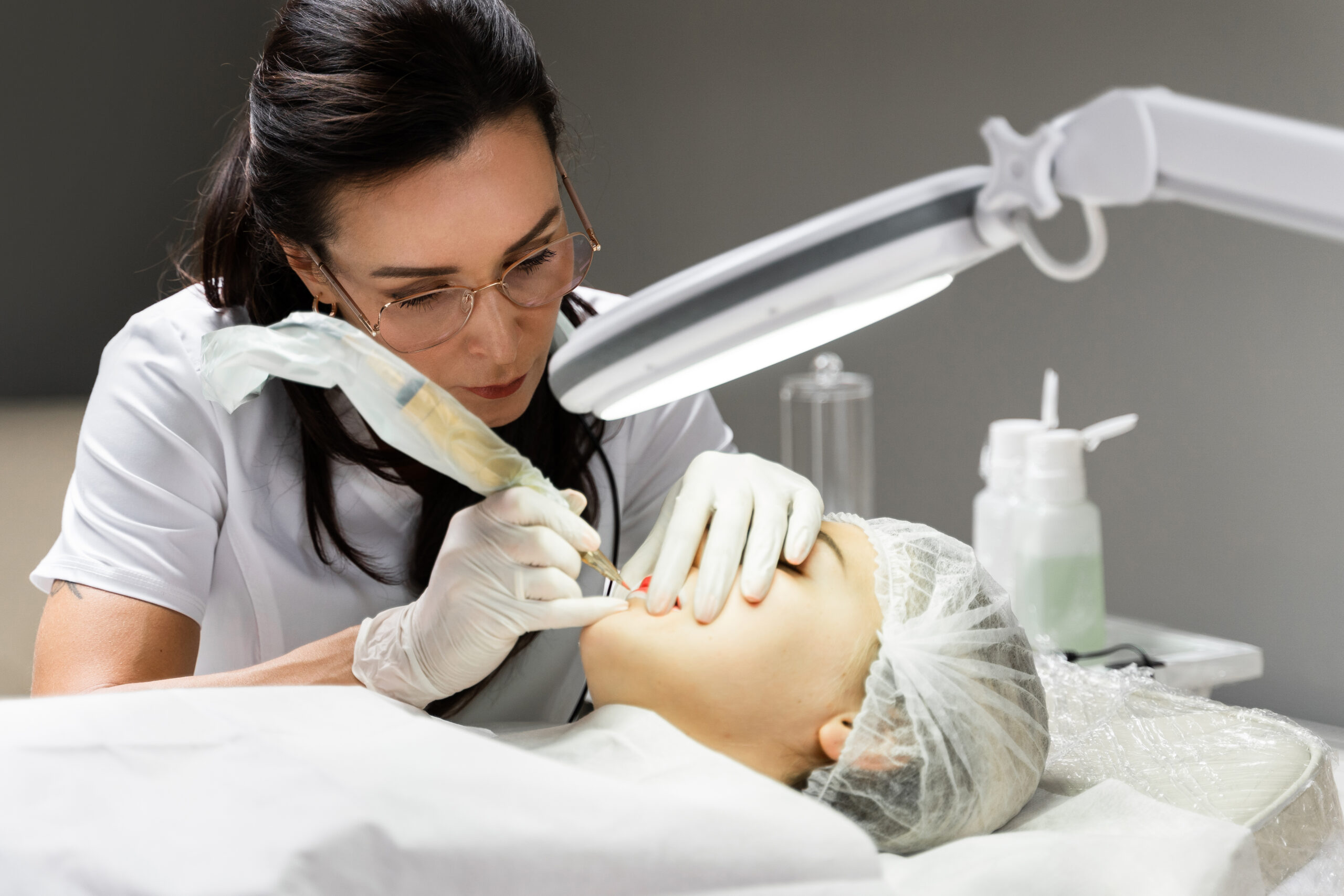 Professional permanent makeup artist and her client during lip blushing procedure